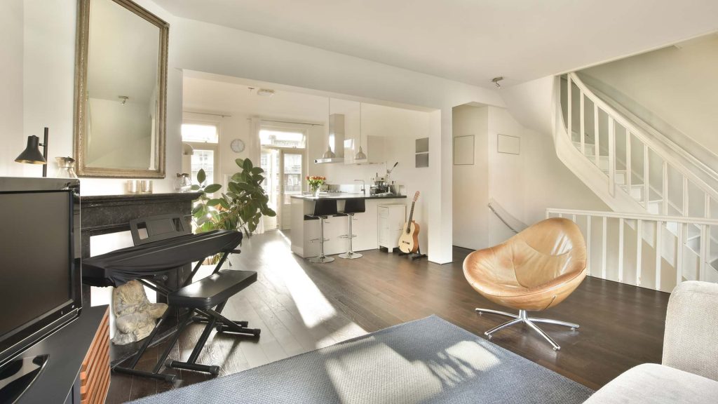 Bright open‑concept living room in a South Lethbridge home showcasing dark hardwood floors, a modern kitchen island with bar stools, leather accent chair, and white spiral staircase.