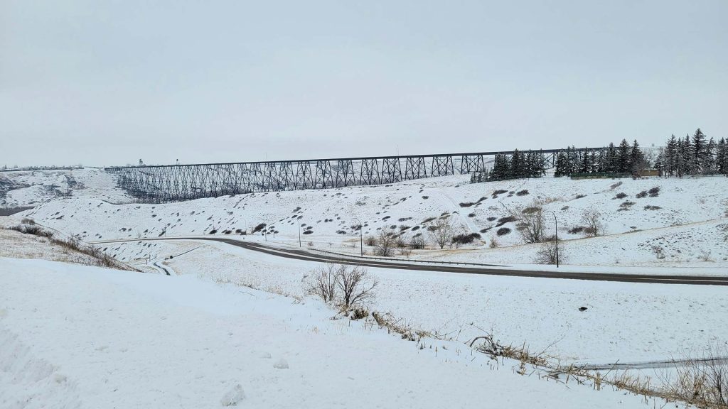 Snow‑covered South Lethbridge coulee with the historic High Level Bridge (Lethbridge Viaduct) spanning the valley above a winding road, showcasing winter scenery near local residential neighbourhoods.